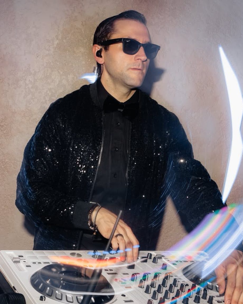 DJ Dayve in a sequin jacket and sunglasses at the decks