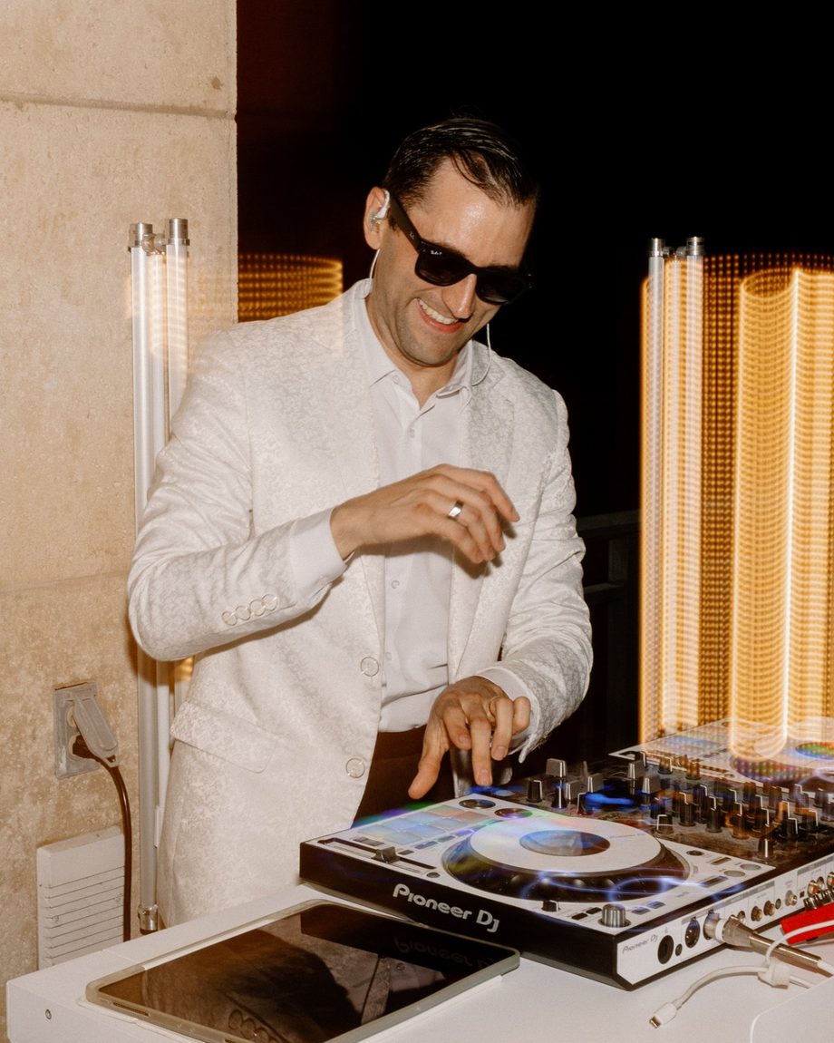 DJ Dayve laughing at the decks in a white jacket